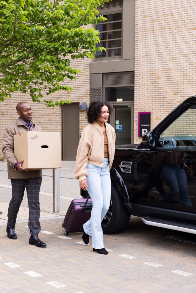 Two people moving luggage next to a car