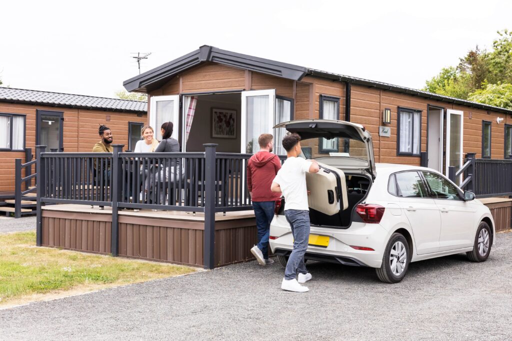 A group of people in a holiday home. Two men are moving luggage out of the car boot.