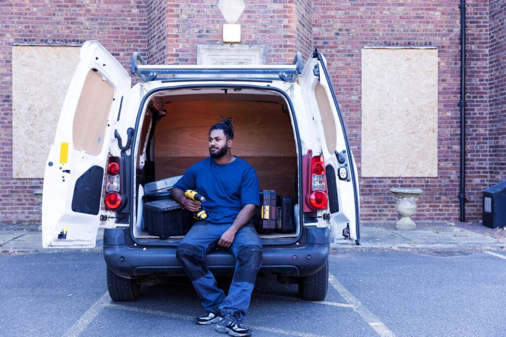 A tradesman holding his drill whilse sitting in the back of his van